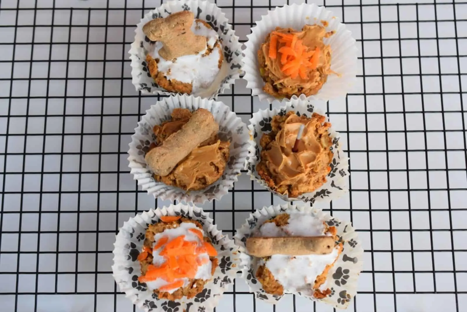 Homemade pup cakes with a variety of topping; carrots, peanut butter and bone treats on metal rack.