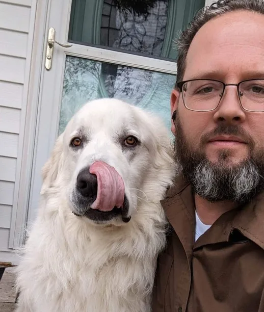 a man takes a picture with a dog that licks itself