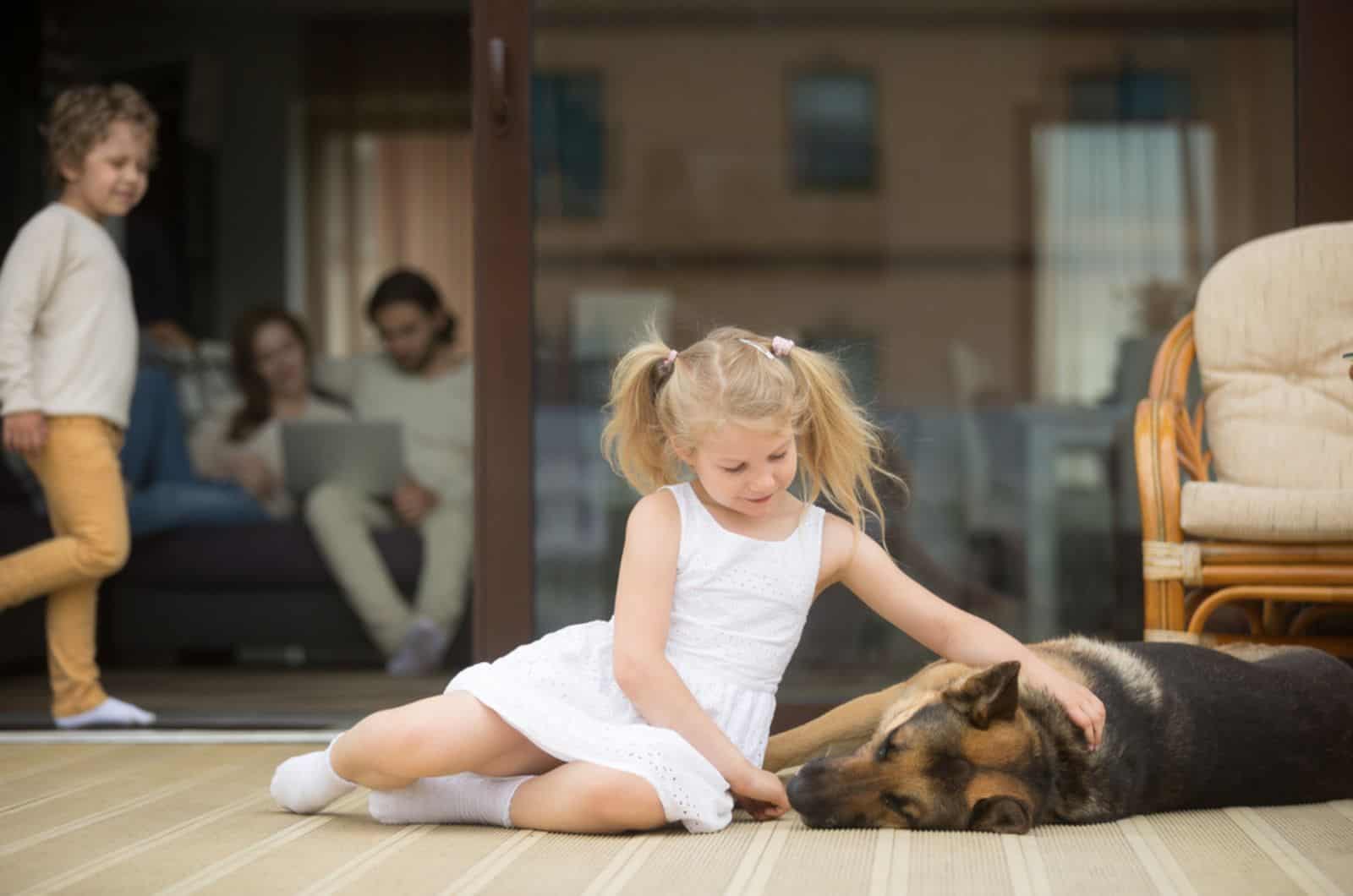 little girl playing with german shepherd dog lying on porch