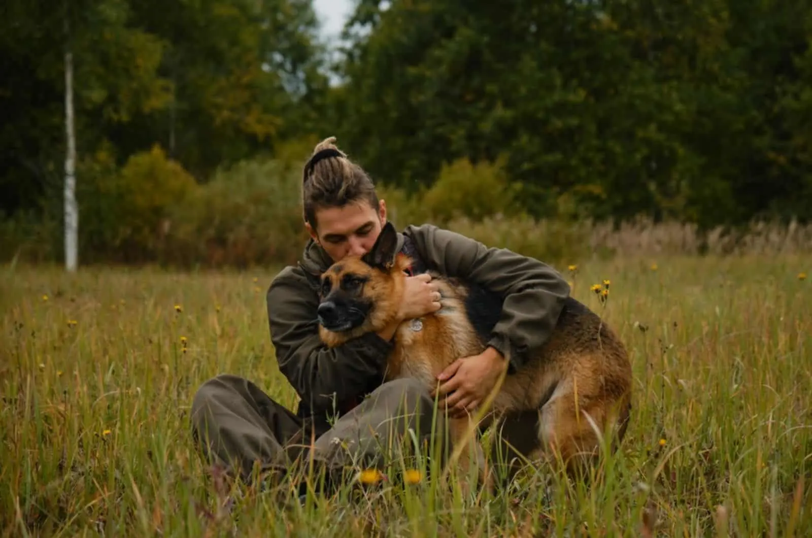 man hugging his german shepherd dog while resting on the grass