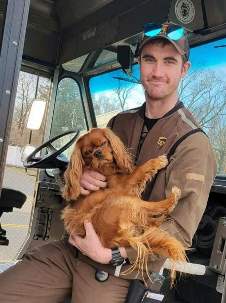 the driver of the UPS is holding a dog in his arms