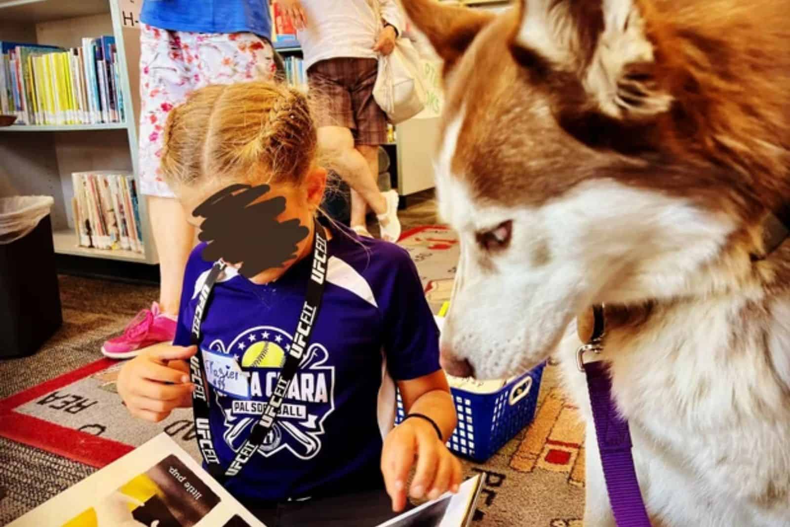 dog sitting beside a little girl while she reading a book