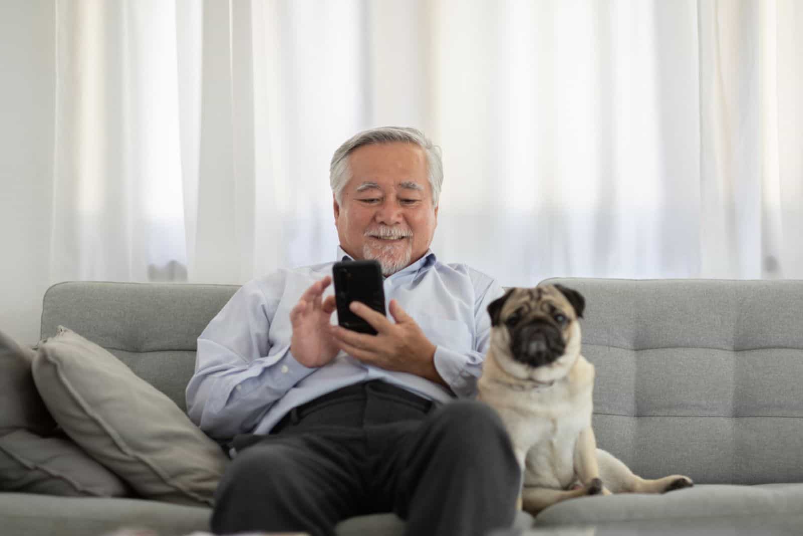 elderly asian man sitting with dog pug on the sofa