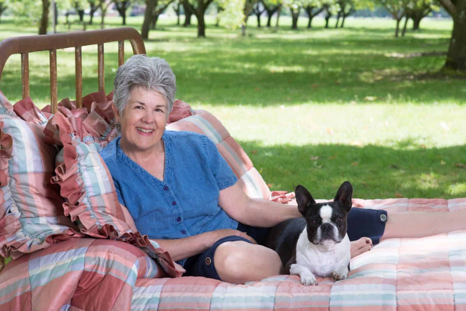 senior woman and her boston terrier lying on an old bed in the yard