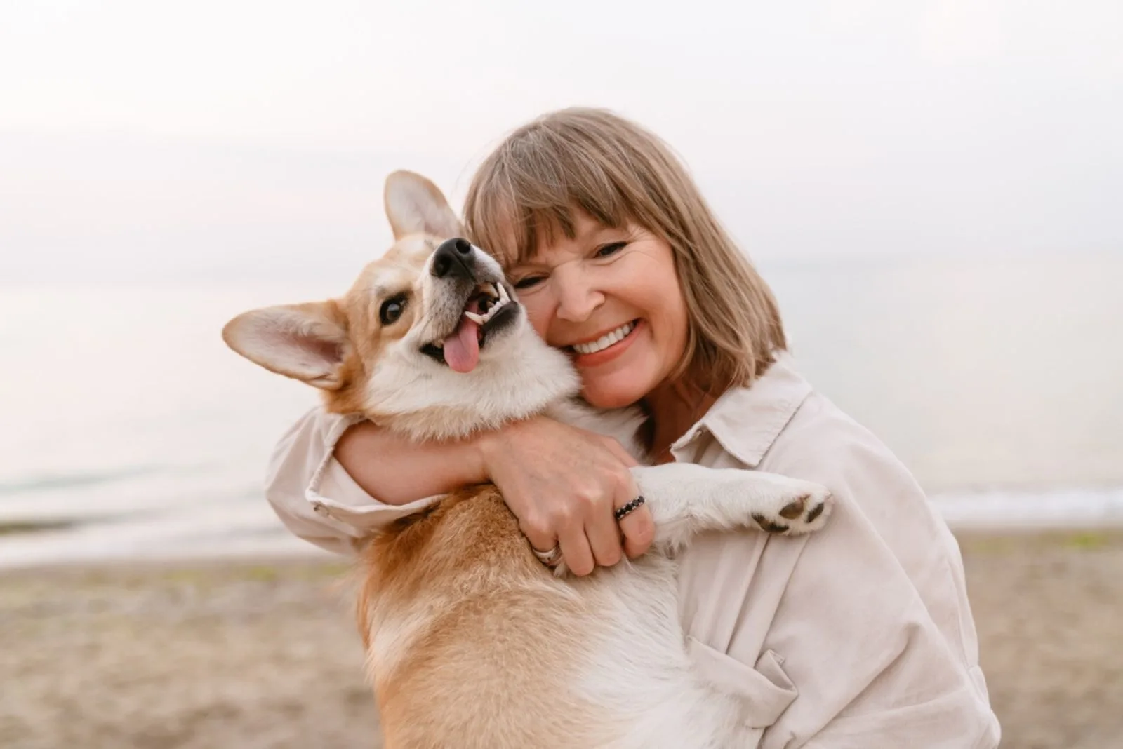 senior woman hugging her corgi dog on the beach
