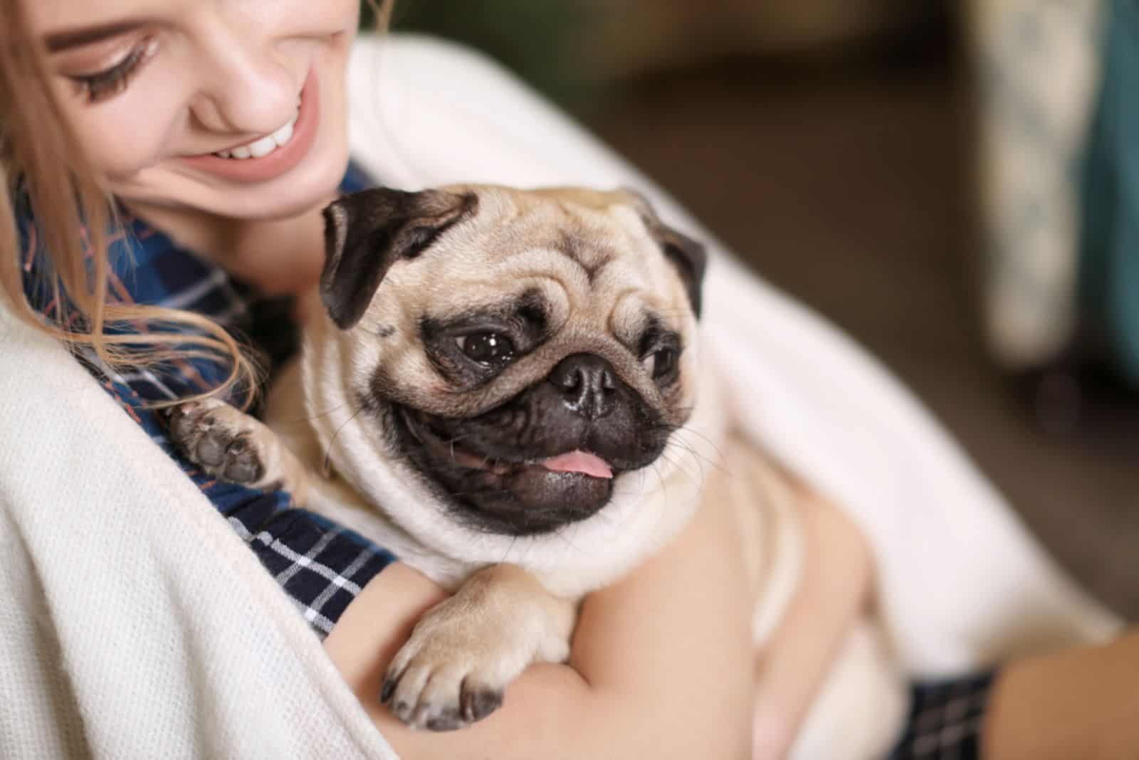 woman holding pug dog in her arms at home