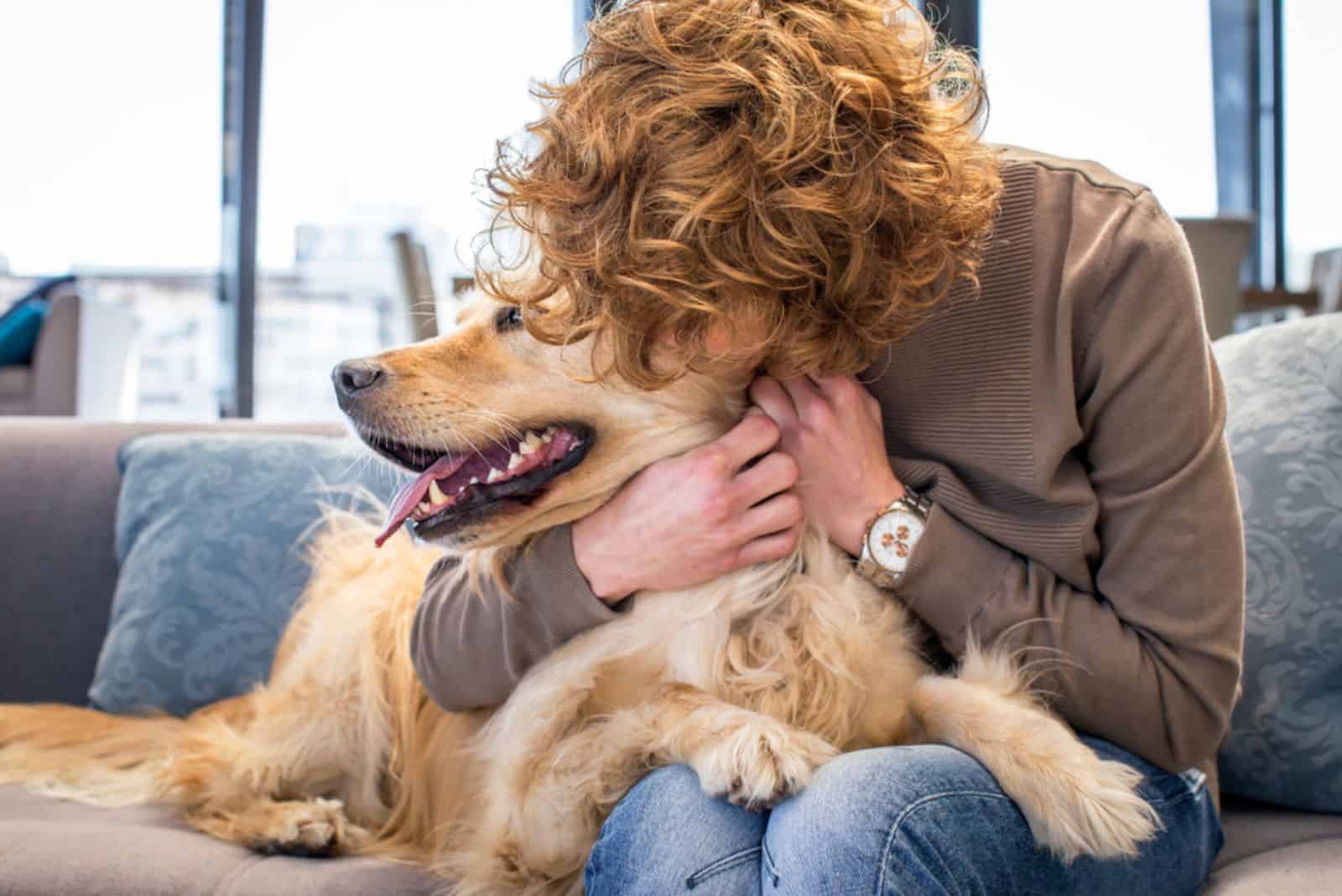 woman kissing and hugging her golden retriever dog on the couch