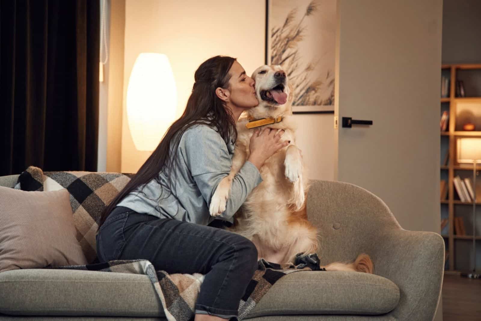 woman kissing her golden retriever dog on the sofa