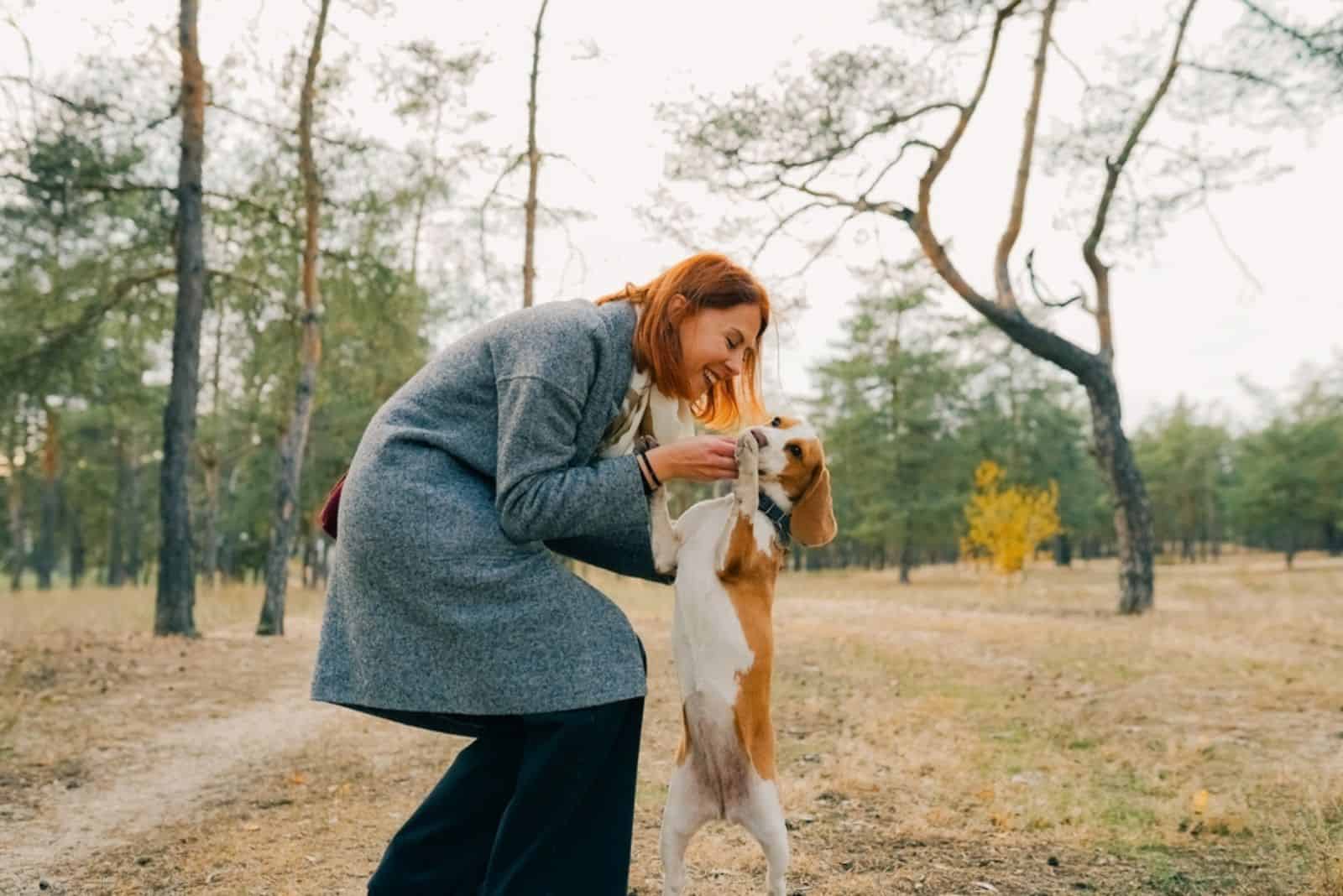 woman with red hair embracing beagle dog in the park