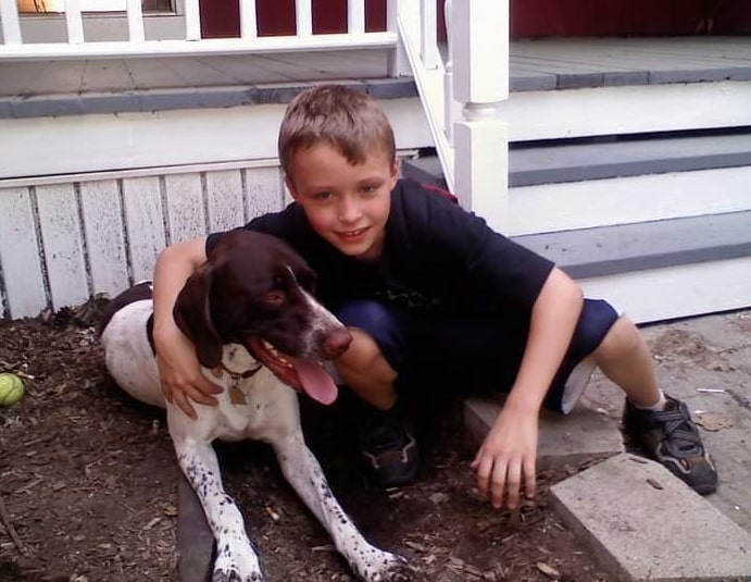 a boy hugs his dog in front of the house in the garden