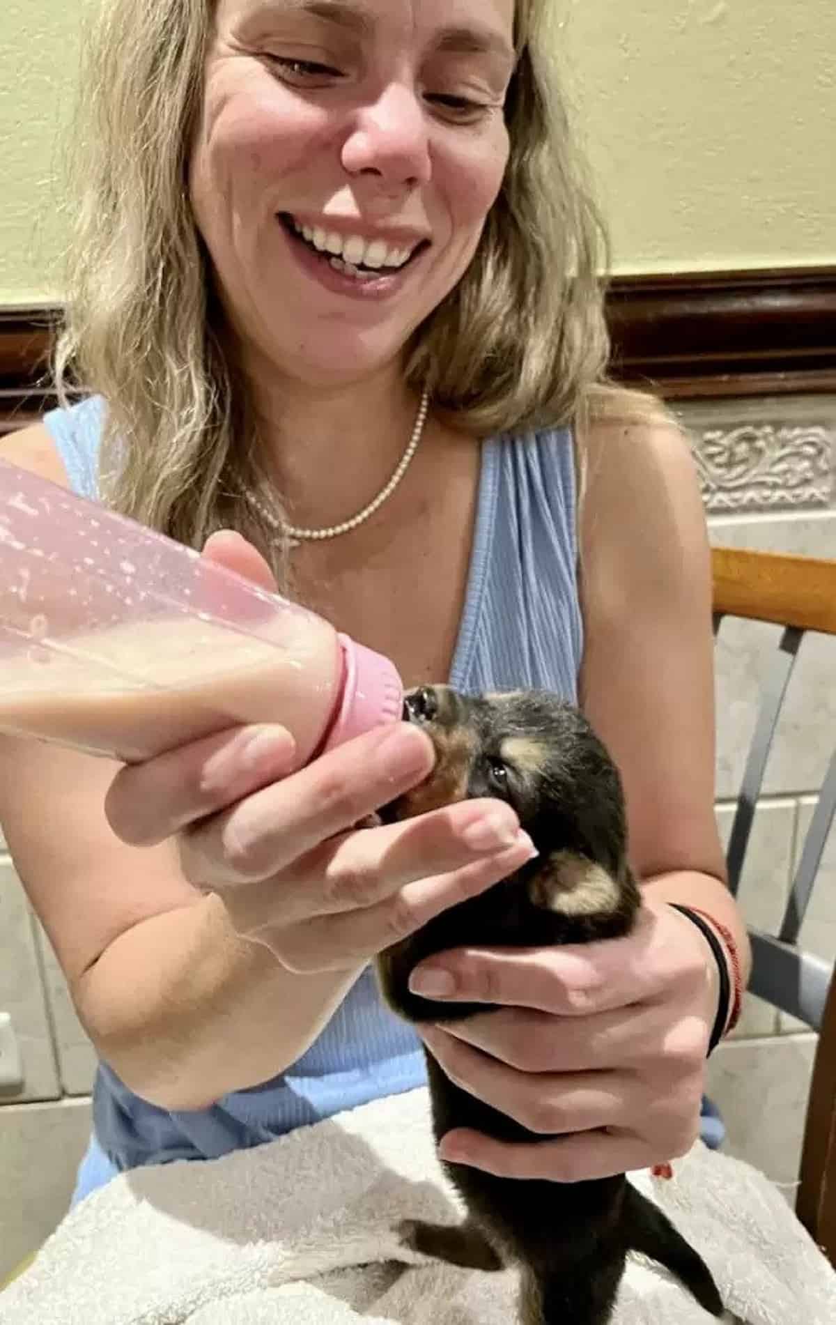 smiling woman feeding a puppy from a bottle