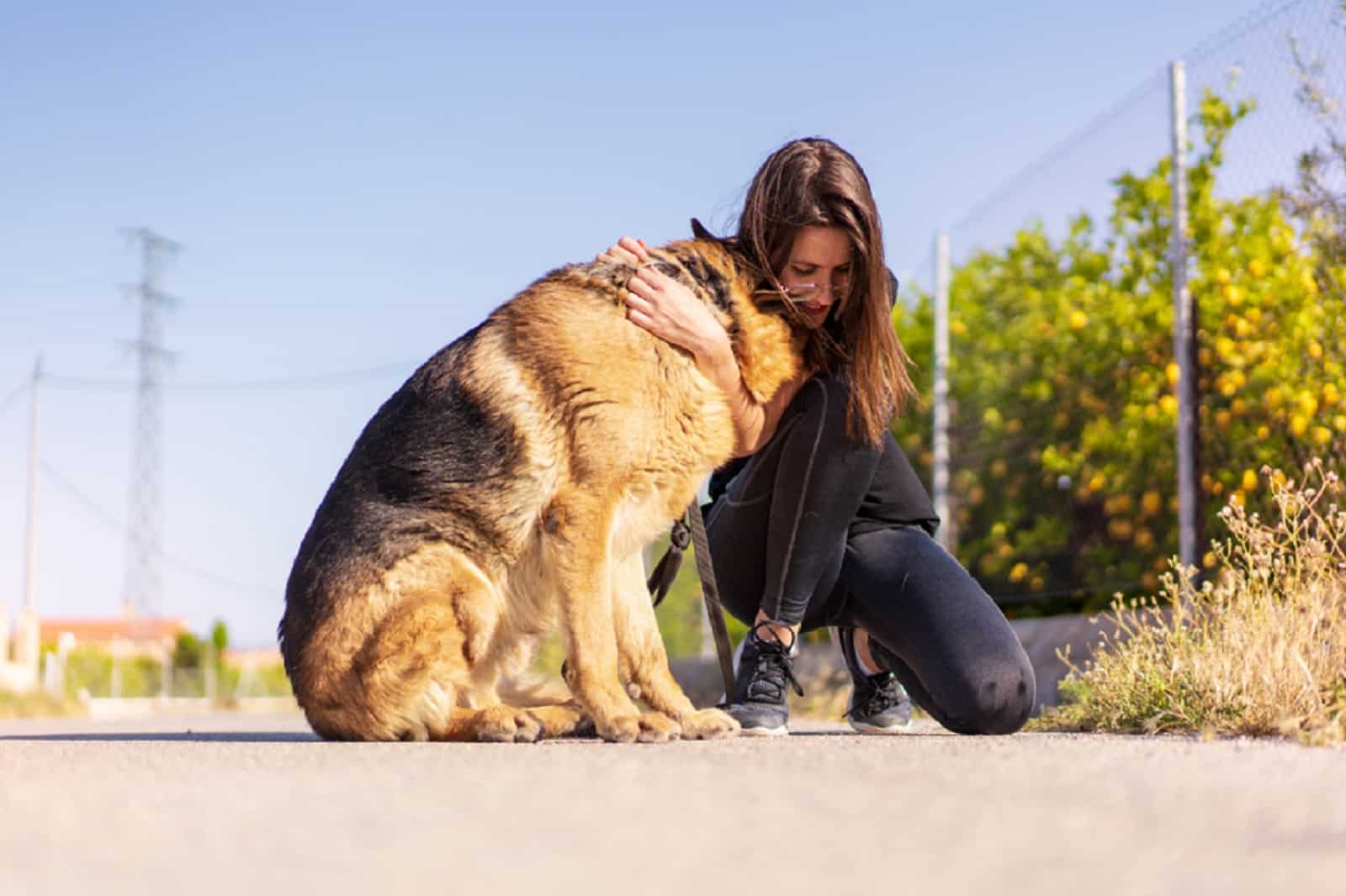 woman hugging her german shepherd dog on the road