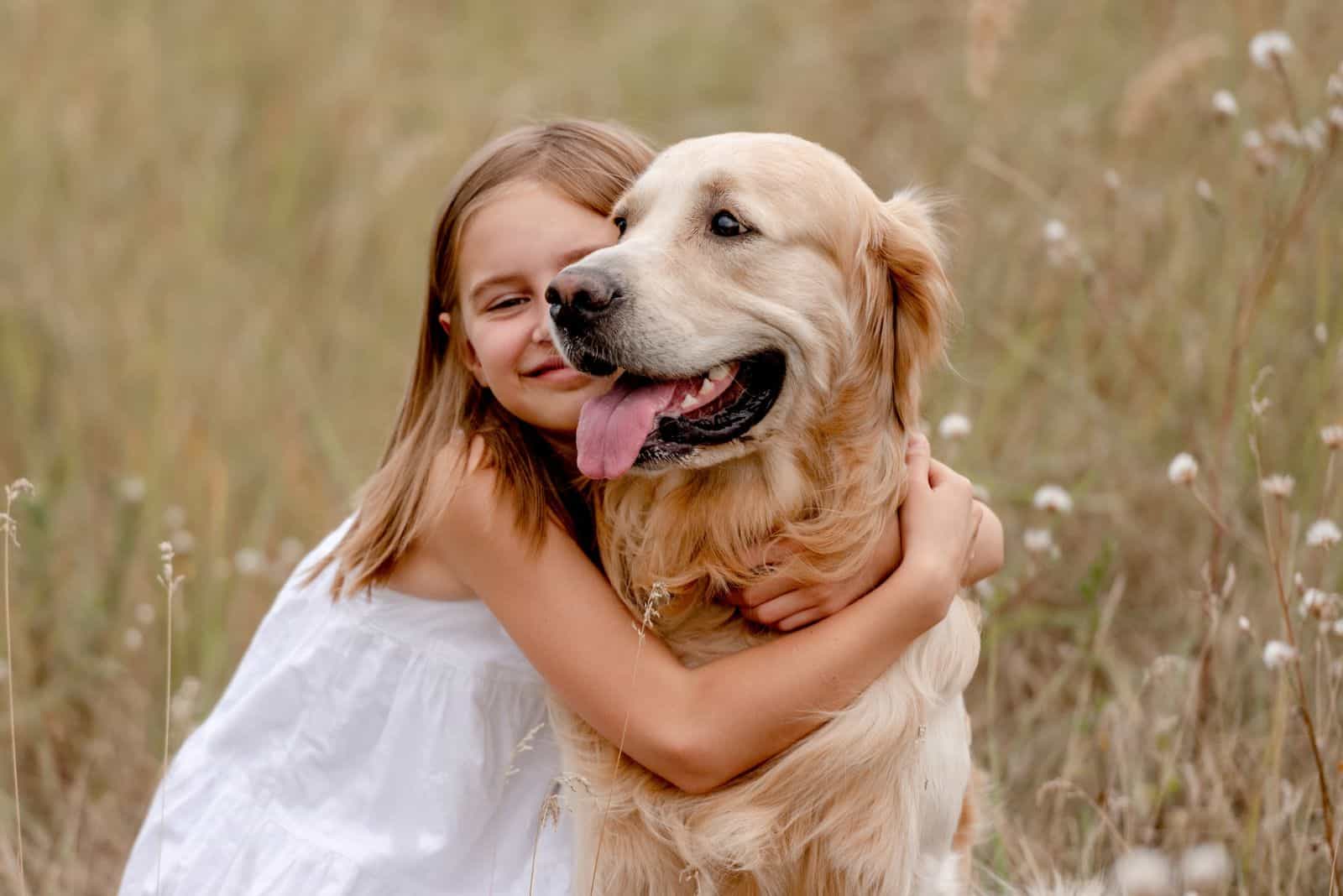 little girl hugging a golden retriever in the field