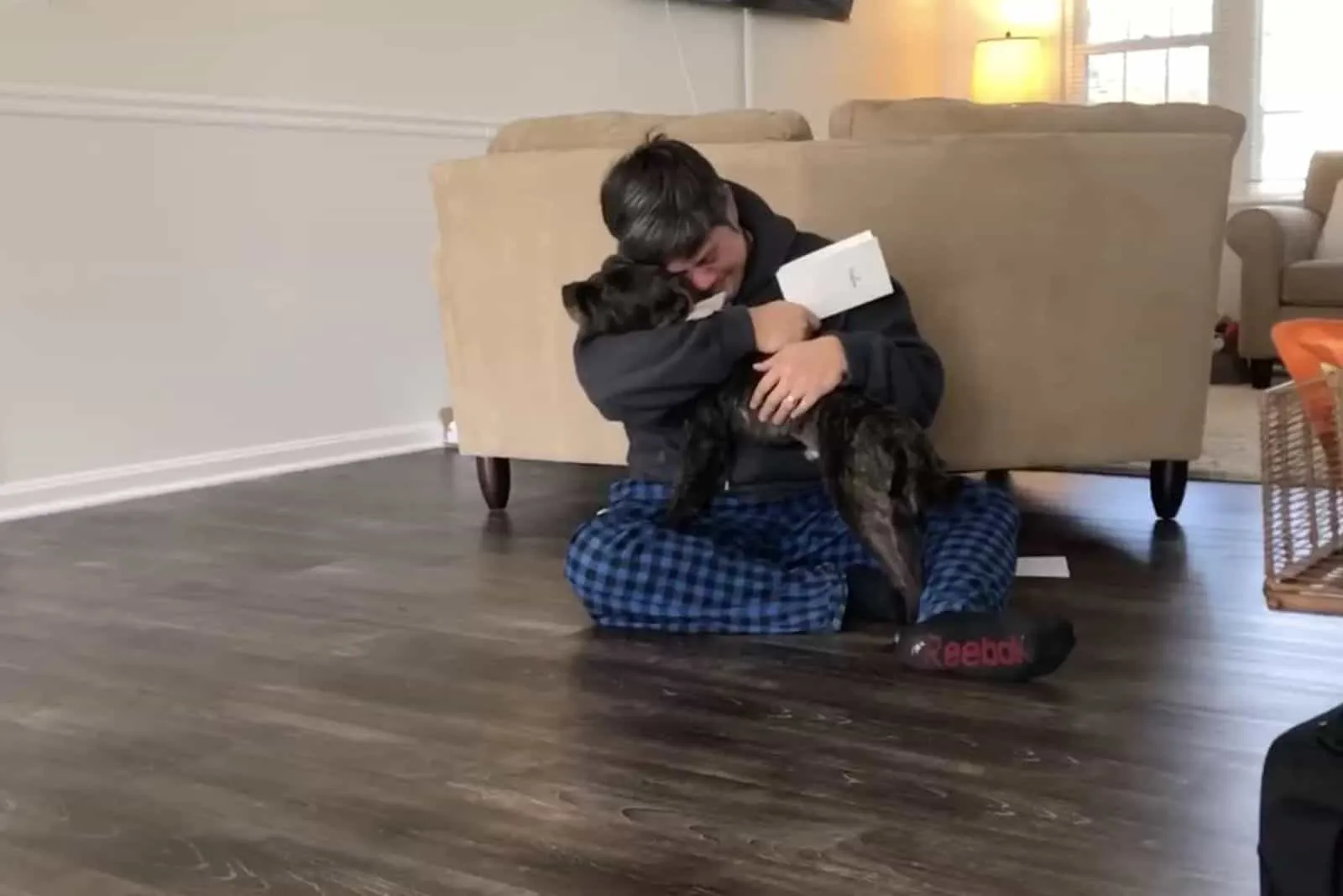 hombre abrazando a un perro negro mientras estaba sentado en el suelo en la sala de estar