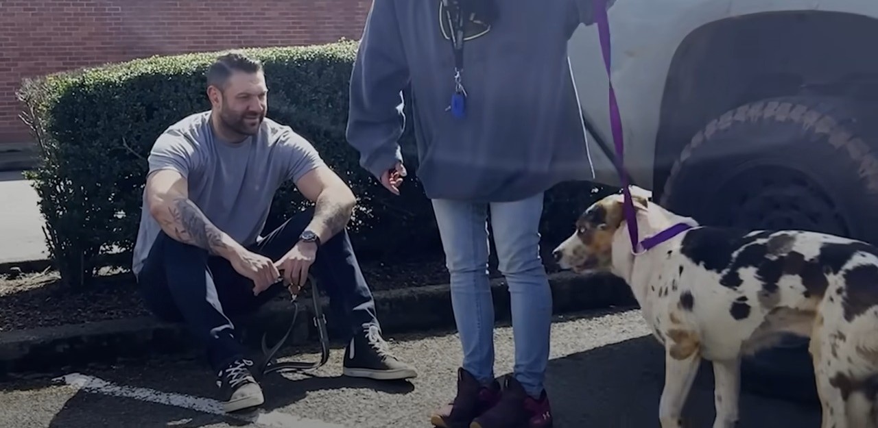 a man is sitting on the sidewalk waiting to be given a dog