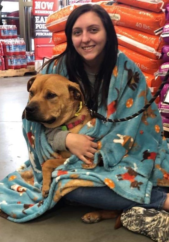 a smiling woman holds a dog wrapped in a blanket in her arms
