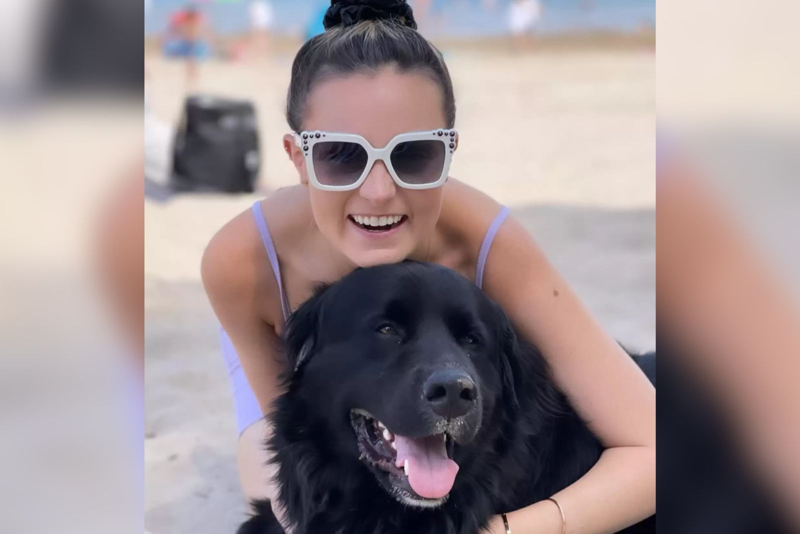 a smiling woman with glasses hugs a black dog