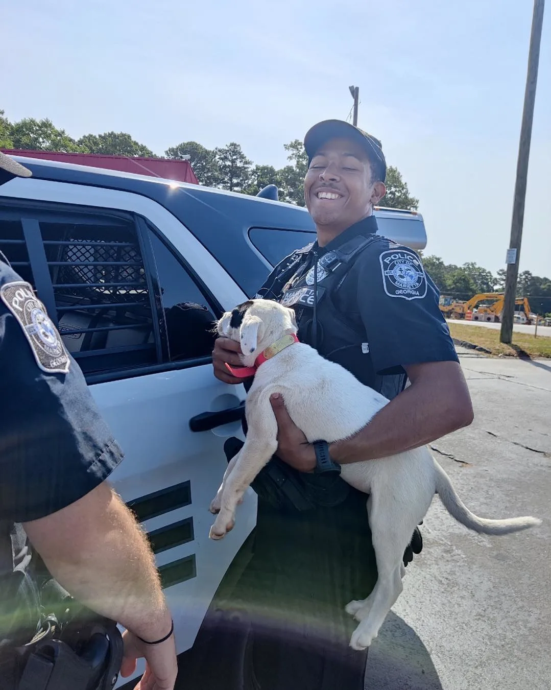 officer holding a puppy and standing next to a police car