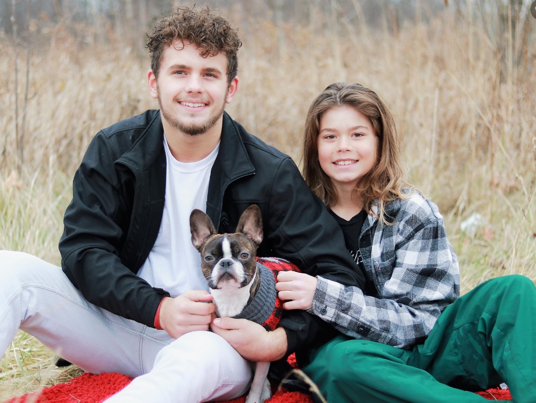 a girl and a boy with a puppy are sitting in a field