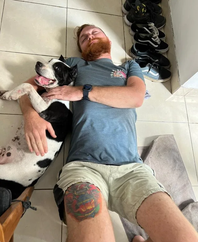 a man hugs a playful dog while lying on the tiles