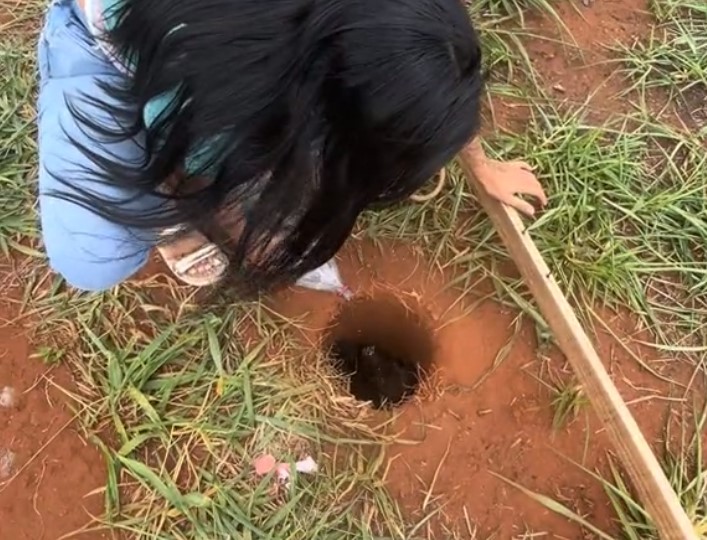 a woman stands next to a dug hole