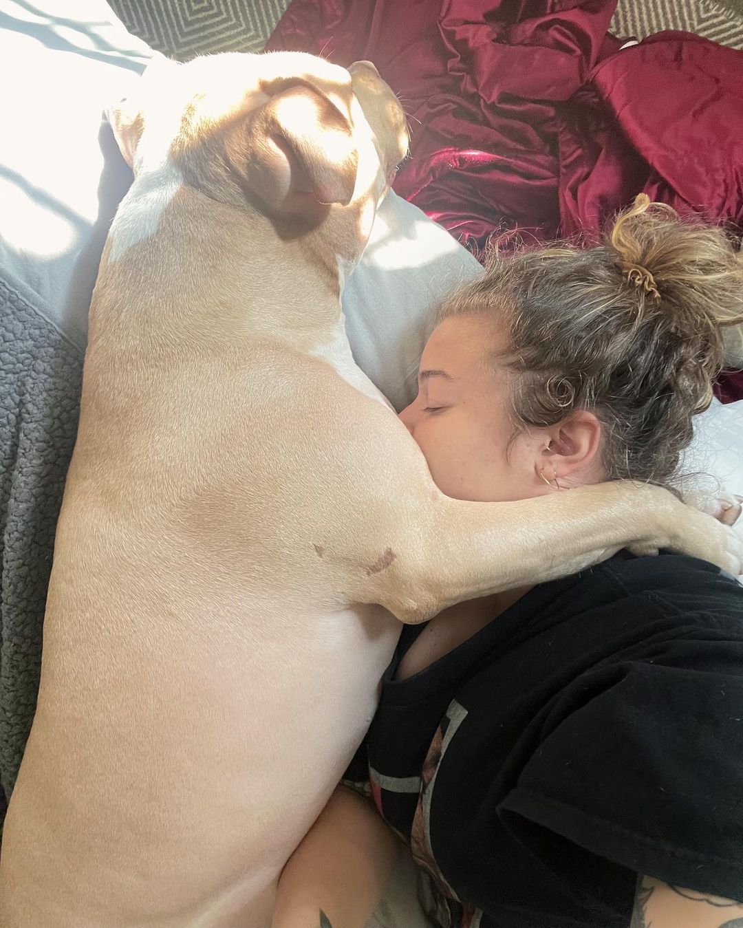 perro abrazando a una mujer mientras está acostado en la cama