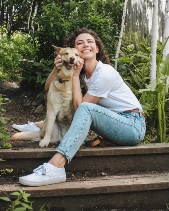 smiling girl sits on wooden steps cuddling with dog