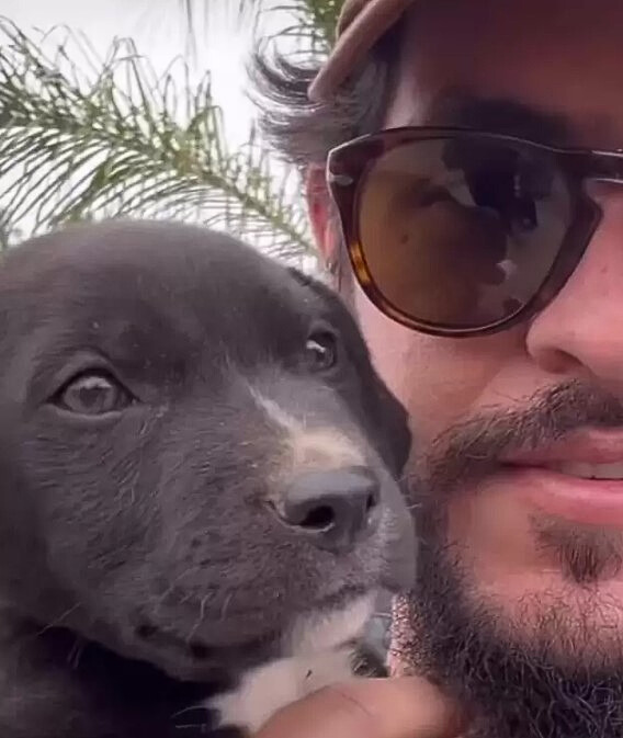 a man with glasses holds a black puppy in his hands