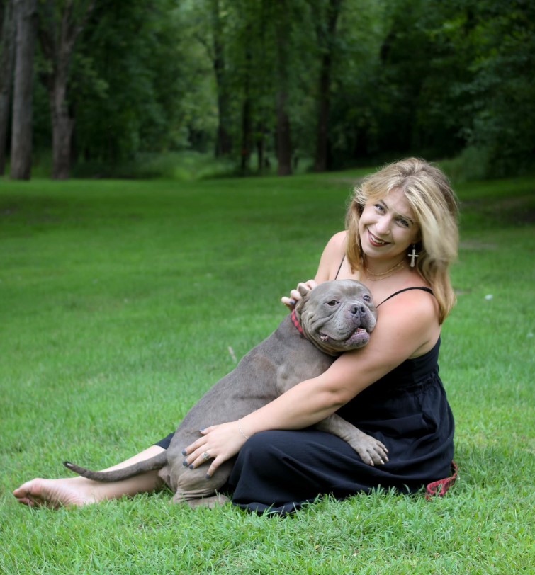 a smiling woman sits on the grass and hugs her dog
