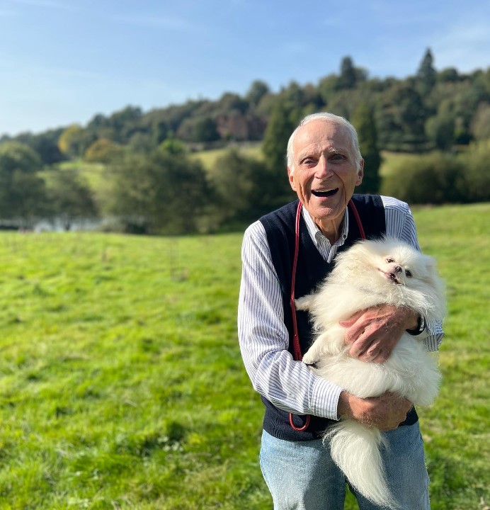 an elderly smiling man holds a dog in his arms