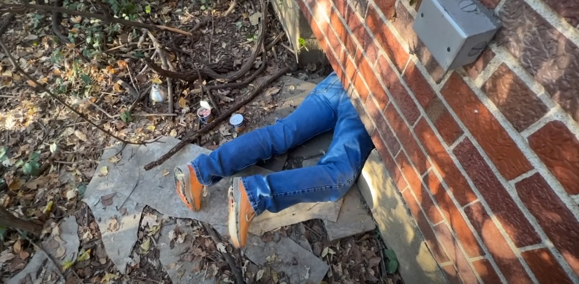 A man crawls under a house