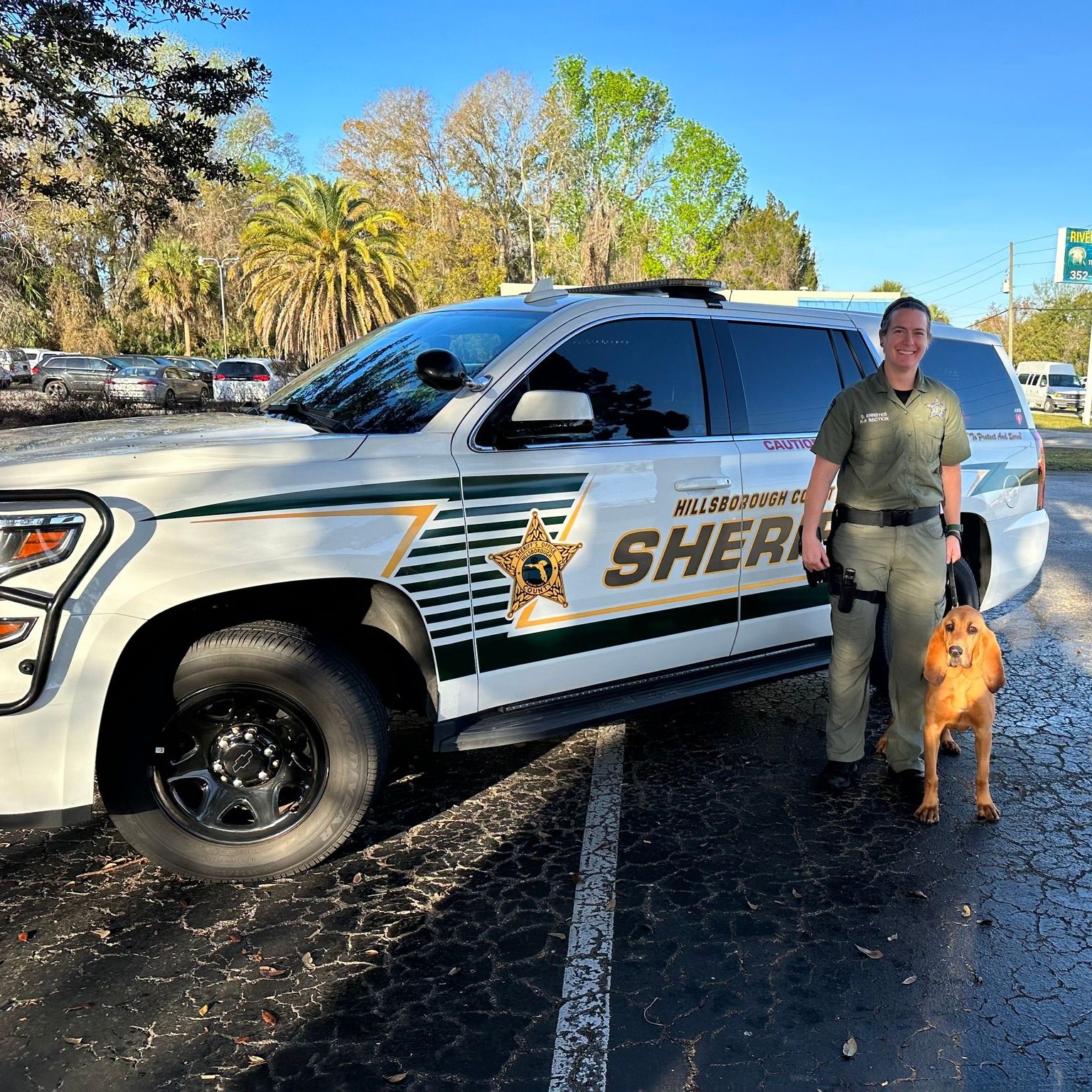 A policewoman takes a picture with her dog next to her car