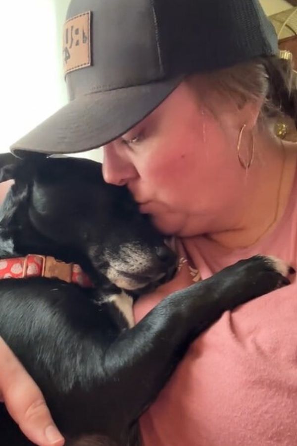 woman kissing a black dog