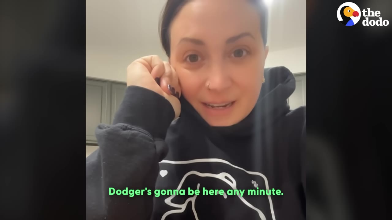 A woman in a black hoodie rests her chin on her hand, looking directly at the camera with an anxious expression as she waits for her foster dog to arrive.