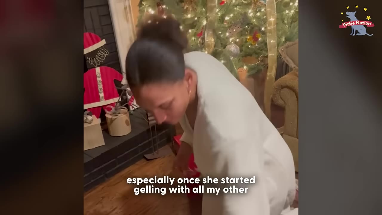 A woman in a white robe leans down in a living room decorated for Christmas, with a Christmas tree in the background.