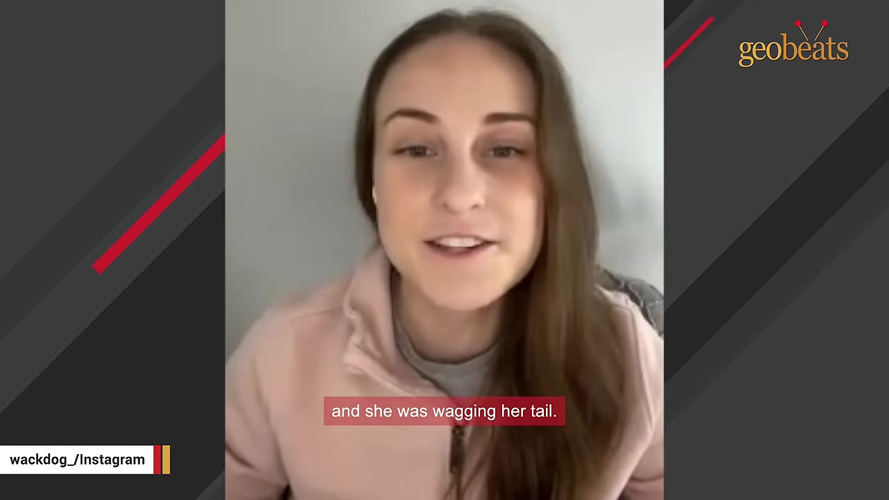A young woman with long brown hair wearing a pink fleece jacket speaks to the camera, with a subtitle that reads 'and she was wagging her tail.'
