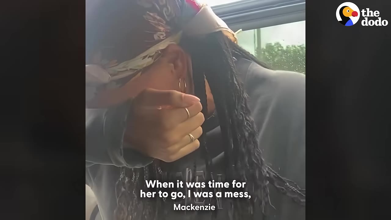 A close-up of a person with braided hair and a headscarf wiping tears from their face inside a vehicle.