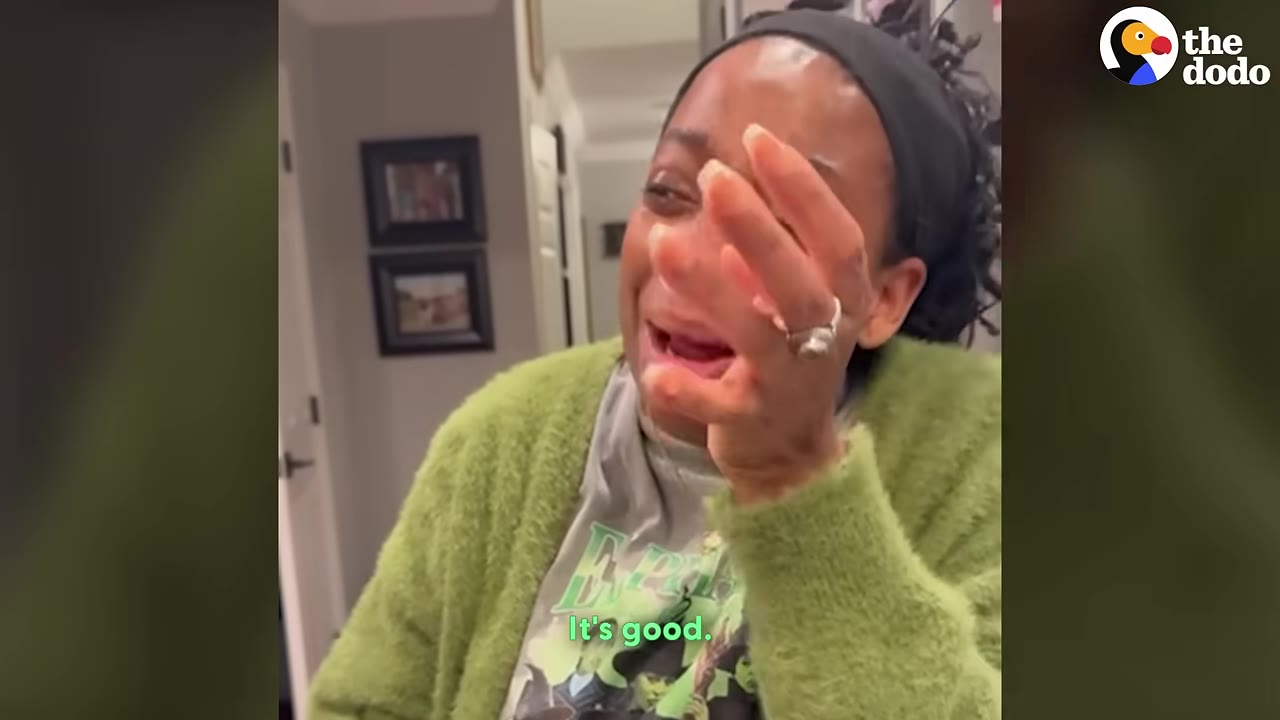 A close-up of a woman wearing a green cardigan and a black headband, crying with tears on her face and covering her mouth with her hand in an emotional moment.