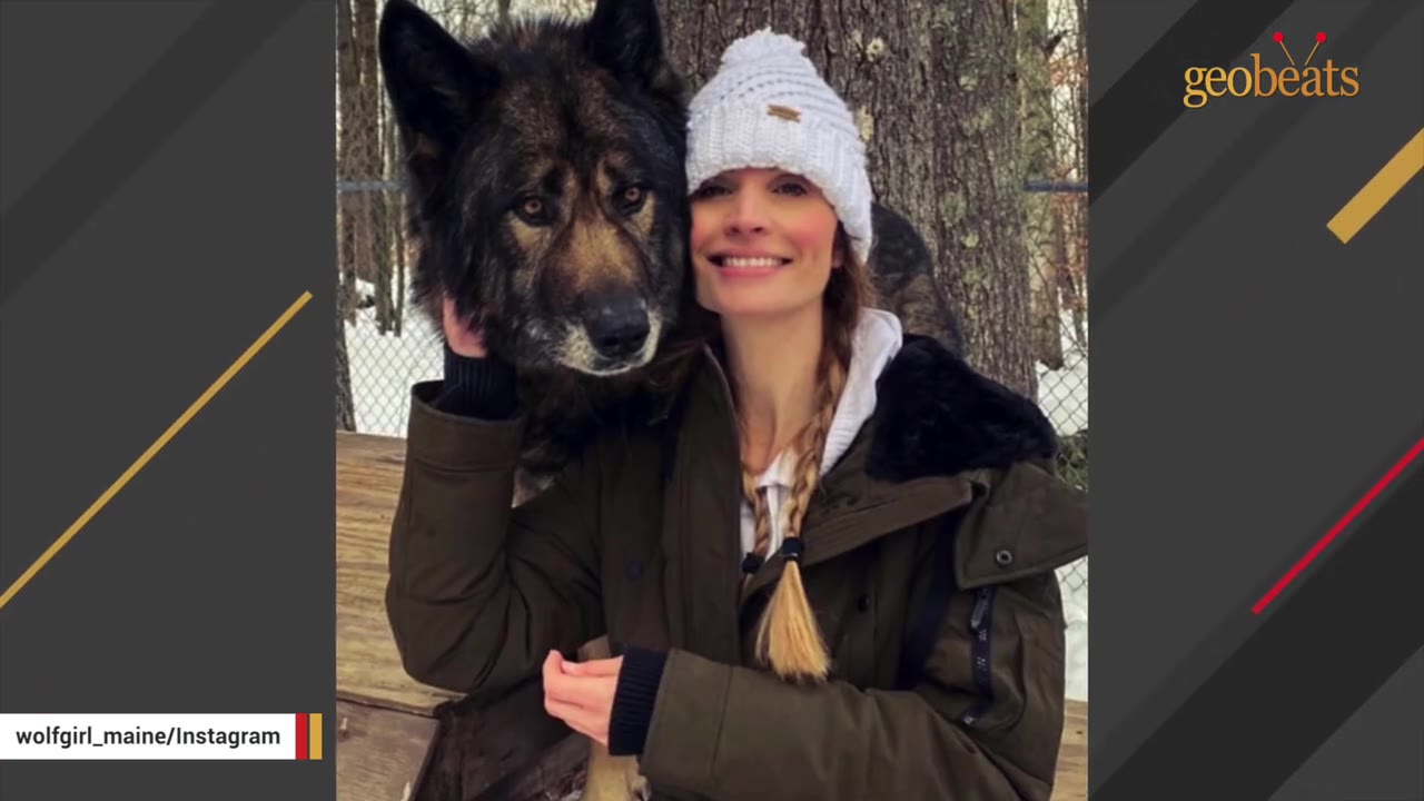 Sarah Hannaford wearing a white beanie and winter coat smiling next to a large wolfdog outdoors in a snowy area.